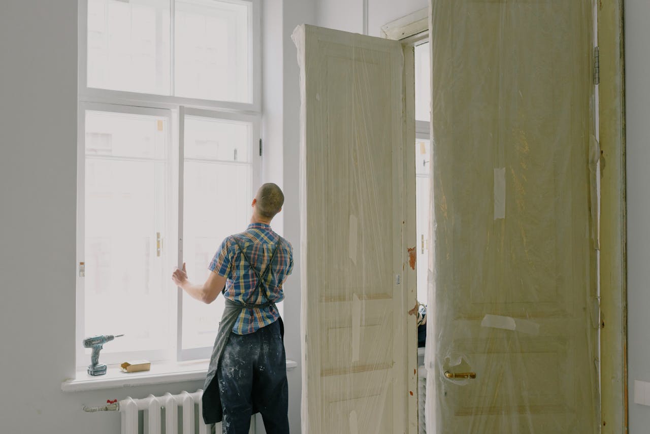 about-02 Back view of unrecognizable workman in apron mounting window near drilling machine and doors in flat