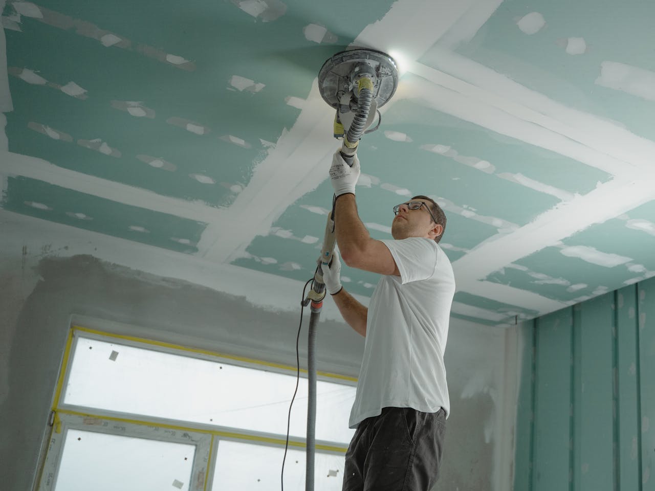 about-01 A professional worker sanding the ceiling during a home renovation project. Indoor construction setting.